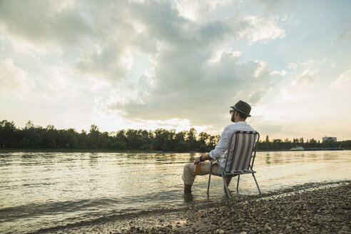 Young man sitting on chair by lakeside - CUF38139