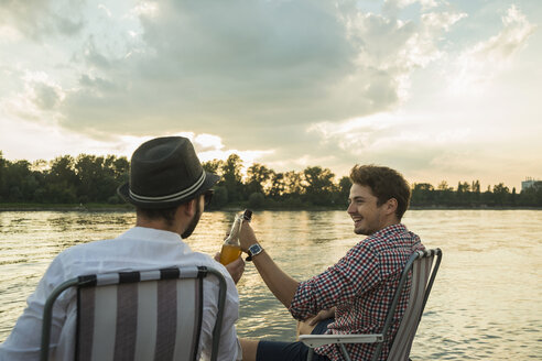 Young men toasting with beer bottles by lake - CUF38140