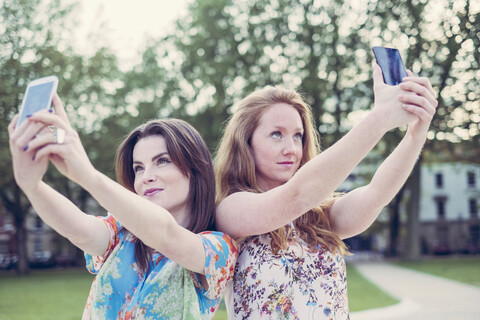 Zwei junge Freundinnen nehmen Selfie auf Smartphones nebeneinander, lizenzfreies Stockfoto