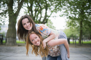 Portrait of two young female best friends giving piggy back in park - CUF38165