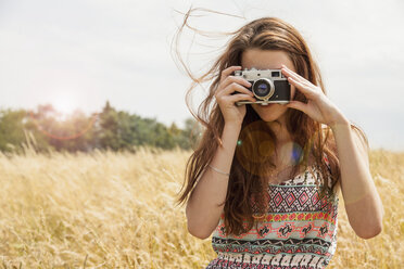 Young woman taking photo with vintage camera in field - CUF38173