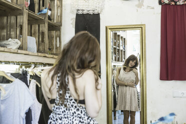 Mid erwachsene Frau hält Kleid vor dem Spiegel in Vintage-Boutique - CUF38179