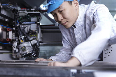 Arbeiter an einer Maschine in einer Fabrik, die auf die Herstellung funktioneller Schaltkreise auf flexiblen Oberflächen spezialisiert ist - CUF38212