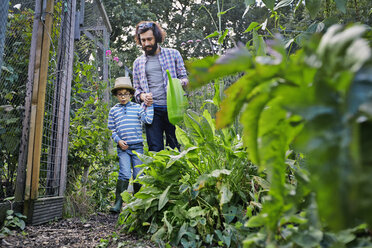 Father and son watering plants on allotment - CUF38260