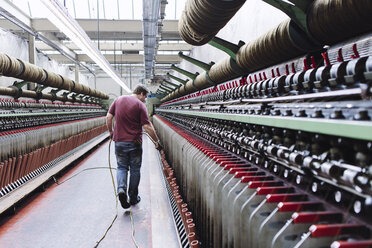 Male factory worker monitoring weaving machines in woollen mill - CUF38376