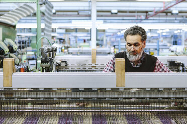 Männlicher Fabrikarbeiter an der Webmaschine in einer Wollspinnerei - CUF38377