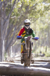 Junger männlicher Motocross-Fahrer, der auf einem Waldstamm fährt - CUF38525