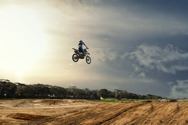 Silhouettierter junger männlicher Motocross-Fahrer, der mitten in der Luft über eine Schlammpiste springt - CUF38528