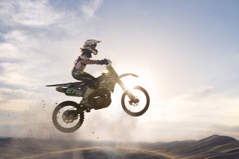 Silhouettierter junger männlicher Motocross-Fahrer, der über eine Schlammpiste springt - CUF38529