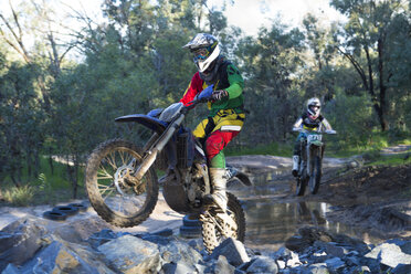 Zwei junge männliche Motocross-Fahrer rasen durch einen Waldfluss - CUF38534