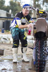 Young male motocross competitor cleaning motorcycle - CUF38542