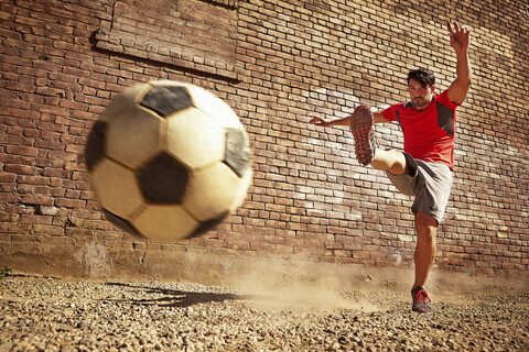 Junger Mann kickt Fußball auf Ödland, lizenzfreies Stockfoto