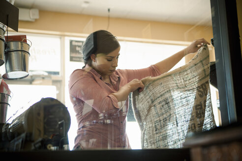 Junge Frau hält einen leeren Sack hoch, der für eine Kaffeeröstmaschine in einem Café verwendet wird - ISF15379