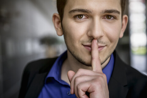Porträt eines jungen Geschäftsmannes mit Finger auf den Lippen im Büro, lizenzfreies Stockfoto