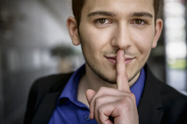 Porträt eines jungen Geschäftsmannes mit Finger auf den Lippen im Büro - ISF15432