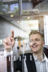 Young businessman writing message on glass wall with finger - ISF15434