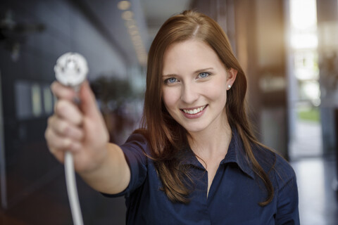 Junge Geschäftsfrau hält Netzkabel im Büro hoch, lizenzfreies Stockfoto