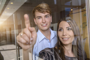 Businesswoman pointing out of glass window to colleague - ISF15452