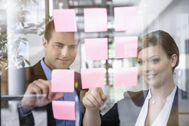 Businessman and woman arranging post it notes on office window - ISF15477
