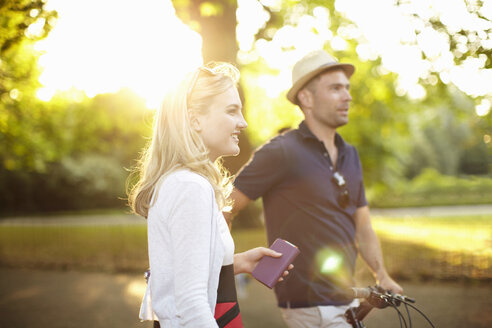 Ehepaar mit Fahrrad in einem sonnenbeschienenen Park spazieren - ISF15571