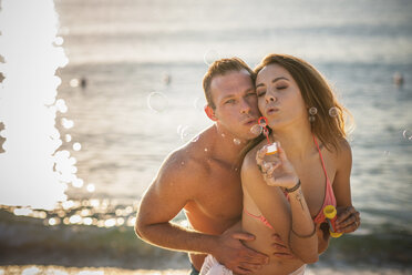 Young couple blowing bubbles on beach, Castiadas, Sardinia, Italy - ISF15573