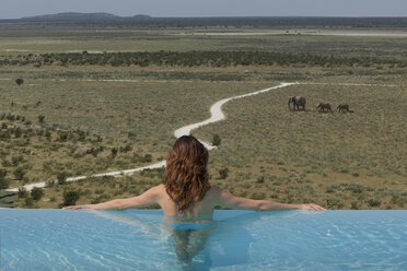 Frau beobachtet Elefanten vom Infinity-Pool im Dolomite Camp, Etosha-Nationalpark, Namibia - CUF38653