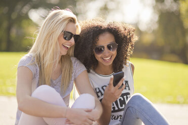 Two young female looking down at text message on smartphone in park - CUF38671