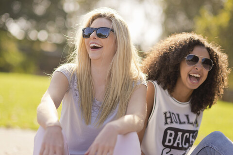 Zwei junge Freundinnen lachen im Park, lizenzfreies Stockfoto