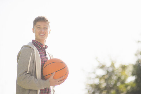 Porträt eines lächelnden jungen Mannes, der einen Basketball hält - CUF38674