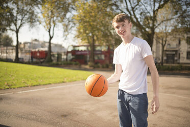 Porträt eines lächelnden jungen männlichen Basketballspielers, der einen Basketball hält - CUF38685