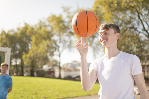Lächelnder junger männlicher Basketballspieler, der den Basketball auf dem Finger balanciert, lizenzfreies Stockfoto