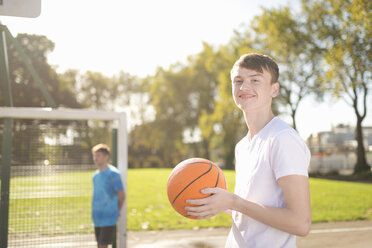 Portrait of smiling young male basketball player on basketball court - CUF38687