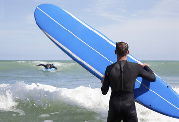 Rückansicht eines männlichen Surfers mit Surfbrett, der einen Freund beim Surfen beobachtet - ISF15647