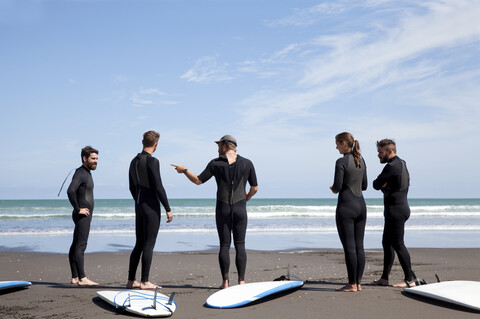 Gruppe von männlichen und weiblichen Surferfreunden, die sich am Strand unterhalten, lizenzfreies Stockfoto