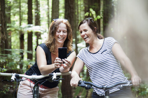 Zwei Mountainbikerinnen schauen im Wald auf ihr Smartphone - ISF15651