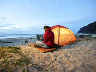 USA, Hawaii, Kauai, Polihale State Park, Frau mit Laptop im Zelt am Strand in der Abenddämmerung - CVF00932