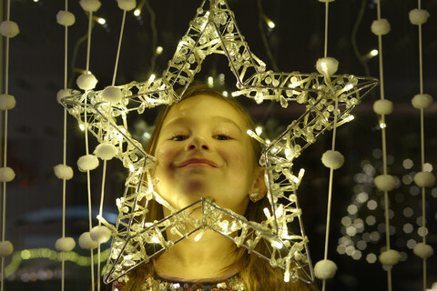 Porträt eines lächelnden kleinen Mädchens, das durch einen Weihnachtsstern schaut, lizenzfreies Stockfoto