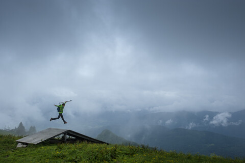 Deutschland, Brauneck, junger Wanderer mit Wanderstöcken und Rucksack springt in die Luft, lizenzfreies Stockfoto