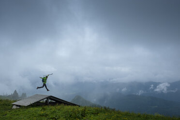 Deutschland, Brauneck, junger Wanderer mit Wanderstöcken und Rucksack springt in die Luft - LBF01997