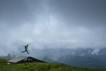 Germany, Brauneck, young hiker with hiking poles and backpack jumping in the air - LBF01997