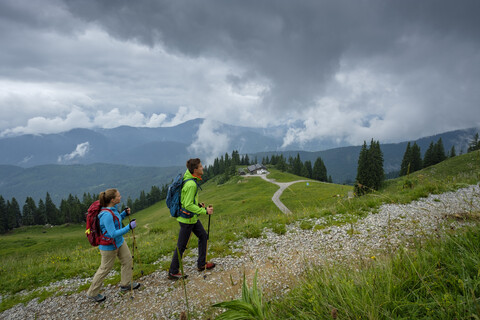 Deutschland, Lenggries, junges Paar mit Wanderstöcken beim Aufstieg, lizenzfreies Stockfoto