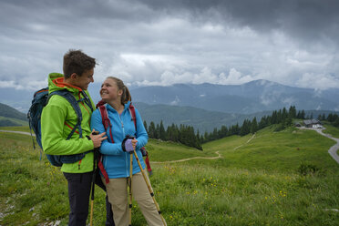 Germany, Lenggries, happy young couple with hiking poles and backpacks on Alpine meadow - LBF02002