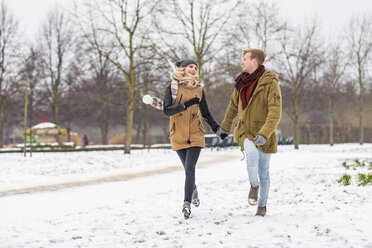 Glückliches junges Paar in der Liebe zu Fuß Hand in Hand in einem Park auf verschneiten Tag - WPEF00569