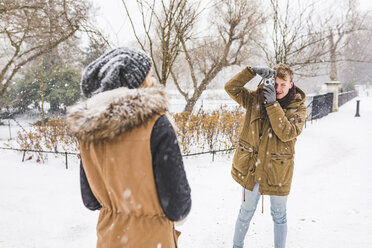 Junger Mann fotografiert seine Freundin im Park an einem verschneiten Tag - WPEF00585