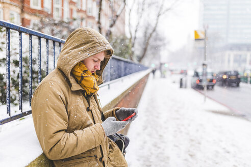 Young man using cell phone outdoors on a snowy day - WPEF00591