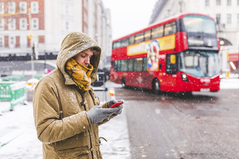 UK, London, young man standing next to the road in the city looking at cell phone - WPEF00594