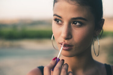 Portrait of teenage girl in nature applying lip gloss - ACPF00073