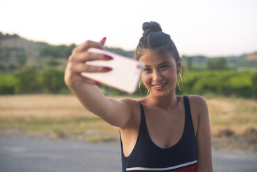 Porträt eines lächelnden Mädchens im Teenageralter, das ein Selfie mit einem Smartphone im Freien macht - ACPF00077