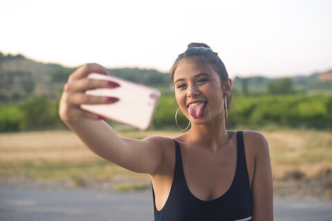 Porträt eines Teenagers, der ein Selfie mit seinem Smartphone macht und dabei die Zunge herausstreckt, lizenzfreies Stockfoto