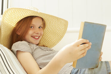 Porträt eines Mädchens, das auf der Veranda einer Ferienwohnung ein Buch liest - CUF38831